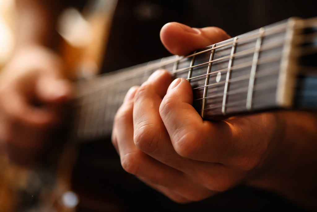 [dark] Detaljeskud af hånd på guitarhals eller klaveranslag i bevægelse—til feature-sektion om teknik, lytning og musikalitet.